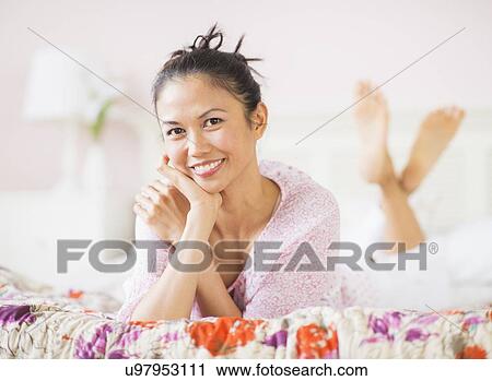 Stock Image - Portrait of mid adult woman lying on bed. Fotosearch