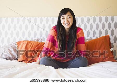 Stock Photograph - Portrait of mid adult woman sitting on bed. Fotosearch