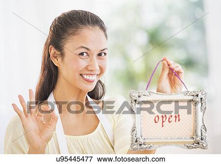 Stock Photo - Portrait of mid adult women holding open sign. Fotosearch