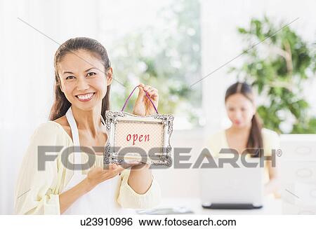 Stock Photograph - Portrait of mid adult women holding open sign. Fotosearch