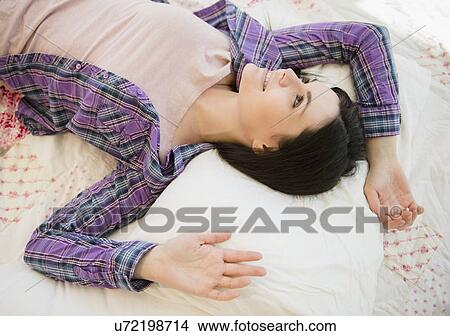 Picture - Portrait of relaxed young woman lying down on bed. Fotosearch