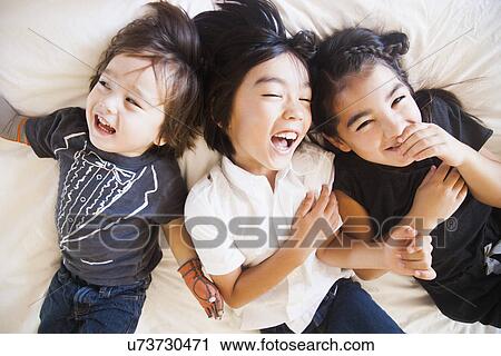 Stock Image - Portrait of siblings laying on bed. Fotosearch
