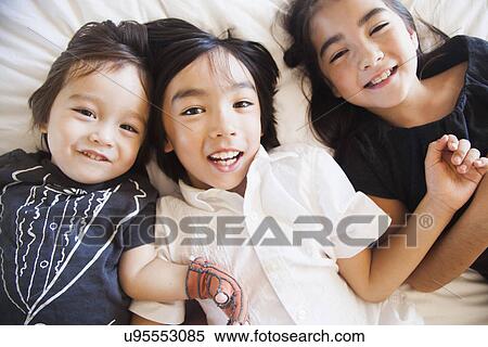 Stock Photography - Portrait of siblings laying on bed. Fotosearch
