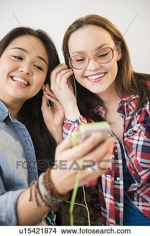 Picture - Portrait of two young women listening to music on MP3 player. Fotosearch