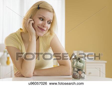 Portrait of woman looking at jar full of money View Large Photo Image Stock Photograph - Portrait of woman looking at jar full of money. Fotosearch