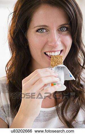 Portrait of young woman eating granola bar View Large Photo Image Stock Photograph - Portrait of young woman eating granola bar. Fotosearch