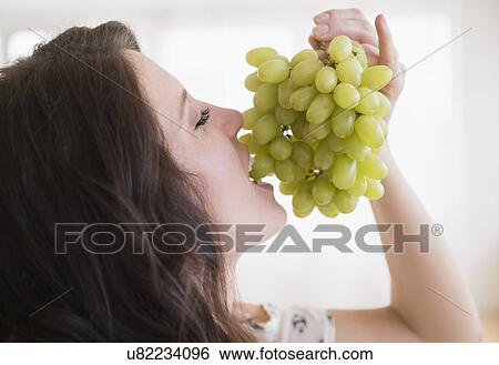 Stock Photograph - Portrait of young woman eating grapes . Fotosearch