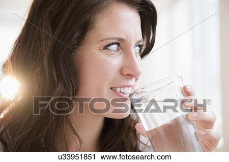 Stock Image - Portrait of young woman holding glass of water. Fotosearch