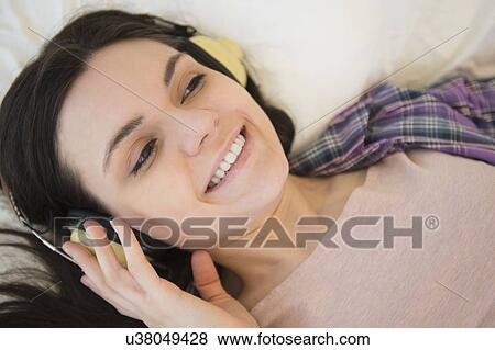 Stock Photo - Portrait of young woman lying down on bed and listening to music. Fotosearch
