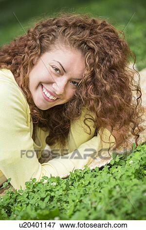Stock Photo - Portrait of young woman lying on grass in park. Fotosearch