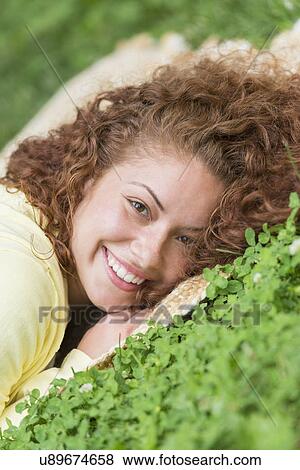 Stock Photo - Portrait of young woman lying on grass in park. Fotosearch