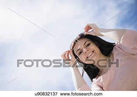 Portrait of young woman standing against cloudy sky View Large Photo Image Stock Photo - Portrait of young woman standing against cloudy sky. Fotosearch