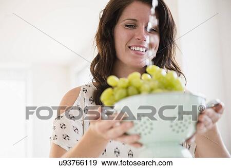 Stock Photo - Portrait of young woman washing grapes in colander. Fotosearch