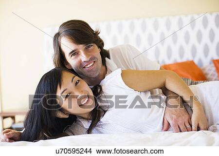 Picture - Pregnant wife with husband cuddling on bed. Fotosearch
