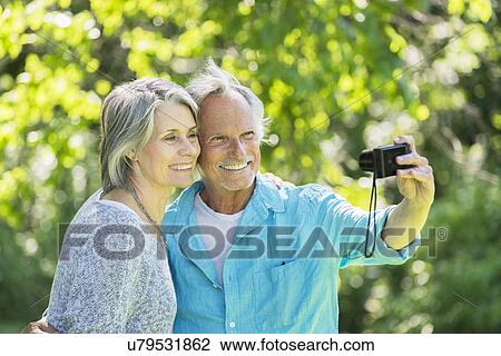 Stock Image - Senior couple photographing themselves in park. Fotosearch