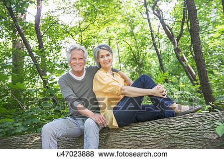 Stock Photo - Senior couple sitting on log in forest. Fotosearch