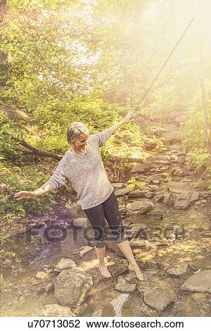 Stock Image - Senior woman crossing stream. Fotosearch
