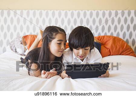 Stock Photograph - Siblings (8-9) using digital tablet in bedroom. Fotosearch