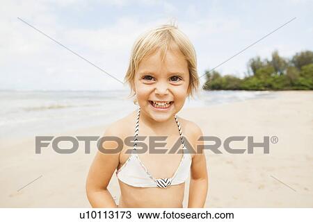 Stock Image - Smiling girl (2-3) on sandy beach. Fotosearch