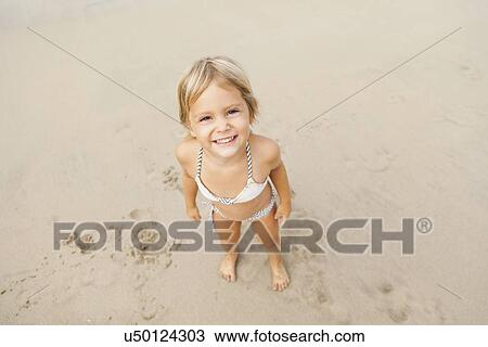 Stock Image - Smiling girl (2-3) on sandy beach. Fotosearch