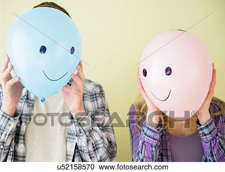 Studio shot of couple holding balloons with smiley faces in front of their heads View Large Photo Image Stock Image - Studio shot of couple holding balloons with smiley faces in front of their heads. Fotosearch