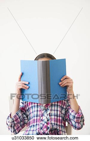 Stock Image - Studio shot of girl (12-13) hiding behind open book. Fotosearch
