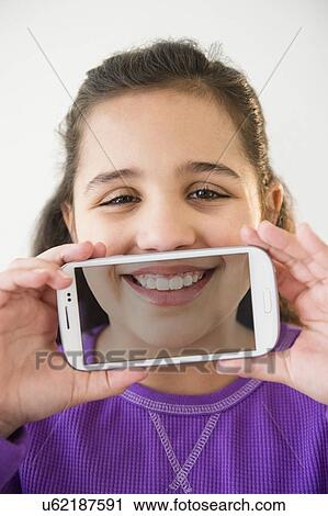 Stock Image - Studio shot of girl (8-9) holding smartphone with picture of her mouth. Fotosearch