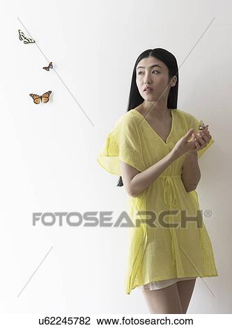 Stock Image - Studio shot of woman looking at butterflies. Fotosearch