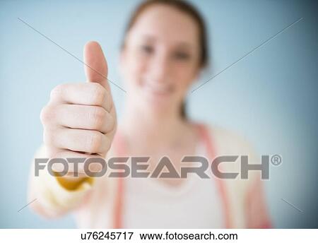 Stock Photo - Teenage girl (14-15) showing thumb up, studio shot. Fotosearch
