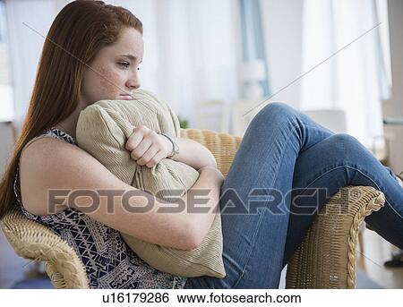 Stock Photograph - Teenage girl (14-15) sitting sad in armchair. Fotosearch