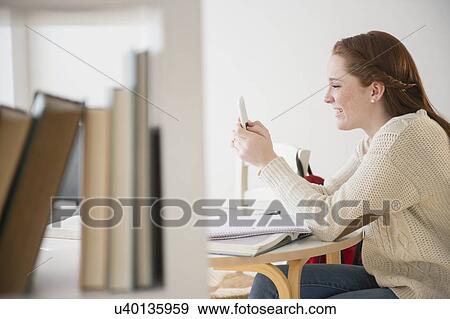 Stock Photo - Teenage girl (14-15) using mobile phone in library. Fotosearch