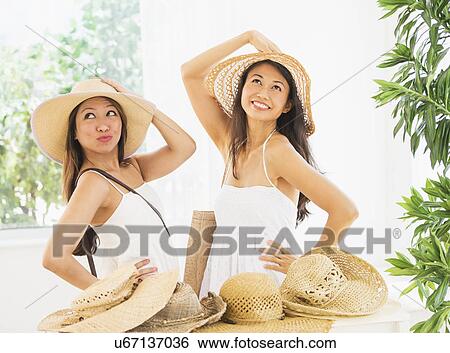 Stock Photograph - Two women trying on straw hat. Fotosearch