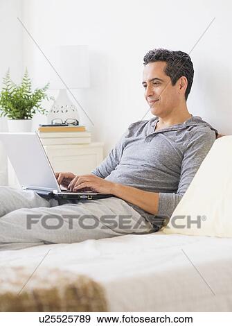 Stock Photo - View of mature man using laptop at home. Fotosearch