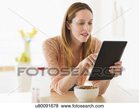 Stock Photo - Woman eating breakfast and looking at tablet pc. Fotosearch