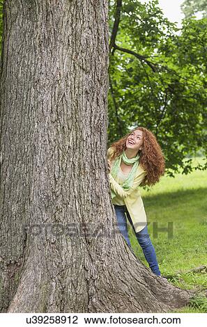 Stock Image - Woman leaning on tree in park. Fotosearch