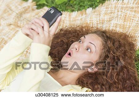 Stock Photography - Woman lying on grass in park and using mobile phone. Fotosearch