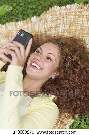 Stock Photography - Woman lying on grass in park and using mobile phone. Fotosearch