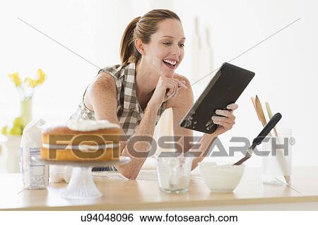 Stock Photograph - Woman using tablet pc in kitchen. Fotosearch