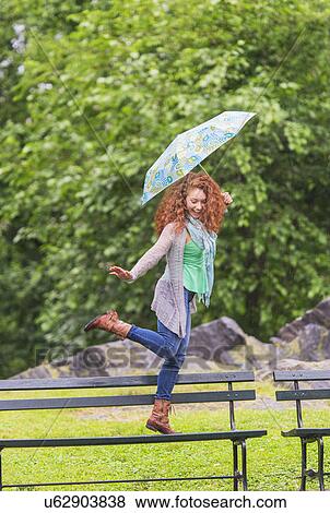 Woman with umbrella dancing on bench in park View Large Photo Image Stock Photo - Woman with umbrella dancing on bench in park. Fotosearch