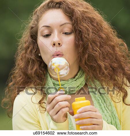 Young woman blowing bubbles in park View Large Photo Image Stock Image - Young woman blowing bubbles in park. Fotosearch