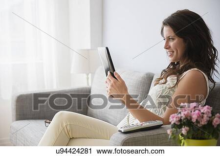 Stock Image - Young woman on sofa reading on digital tablet. Fotosearch