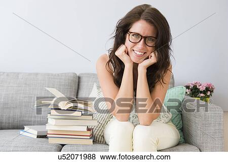Young woman sitting on sofa next to stack of books View Large Photo Image Stock Photo - Young woman sitting on sofa next to stack of books. Fotosearch