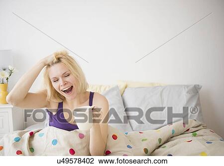 Stock Image - Young woman yawning in bed. Fotosearch