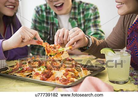 Young women and man eating nachos with melted cheese View Large Photo Image Stock Image - Young women and man eating nachos with melted cheese. Fotosearch