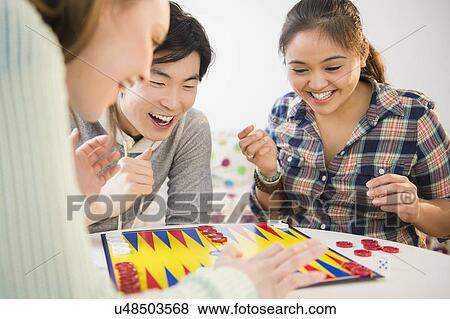 Stock Photo - Young women and man playing backgammon. Fotosearch