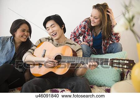 Young women listening to man playing guitar View Large Photo Image Stock Image - Young women listening to man playing guitar. Fotosearch