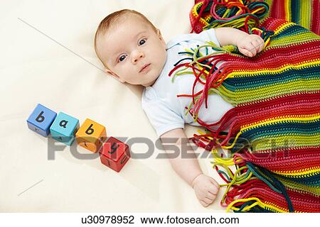 Stock Image - Baby boy lying under striped blanket with blocks spelling baby. Fotosearch