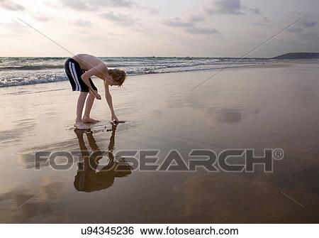 Boy bending over touching sand on beach View Large Photo Image Stock Photograph - Boy bending over touching sand on beach. Fotosearch