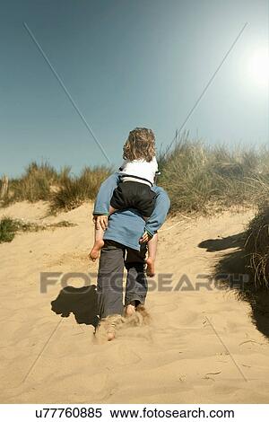 Boy giving girl piggy back over sand dunes View Large Photo Image Stock Photography - Boy giving girl piggy back over sand dunes. Fotosearch