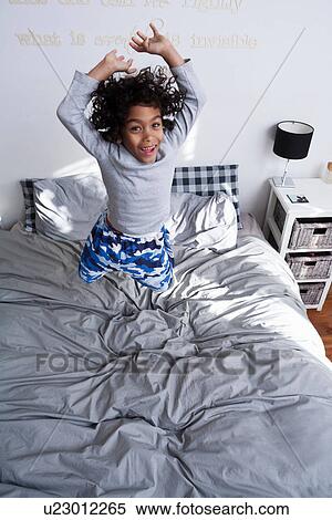 Stock Photography - Boy jumping on bed with arms up. Fotosearch